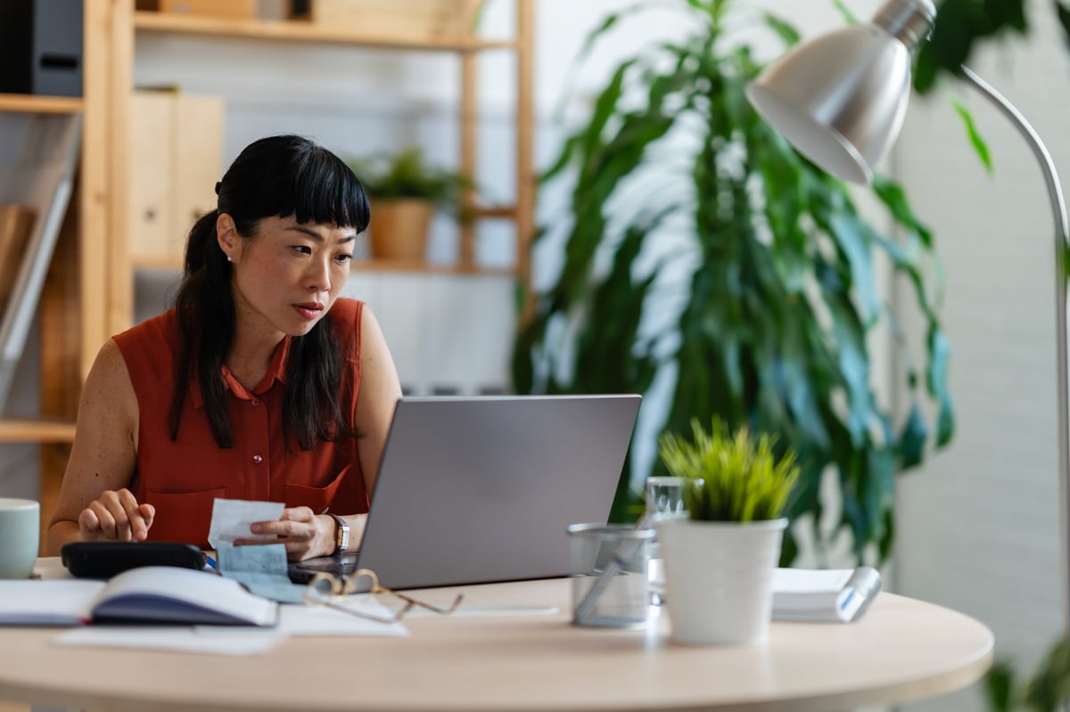 Mujer emprendedora revisando gastos en su computadora, con calculadora y recibos sobre el escritorio