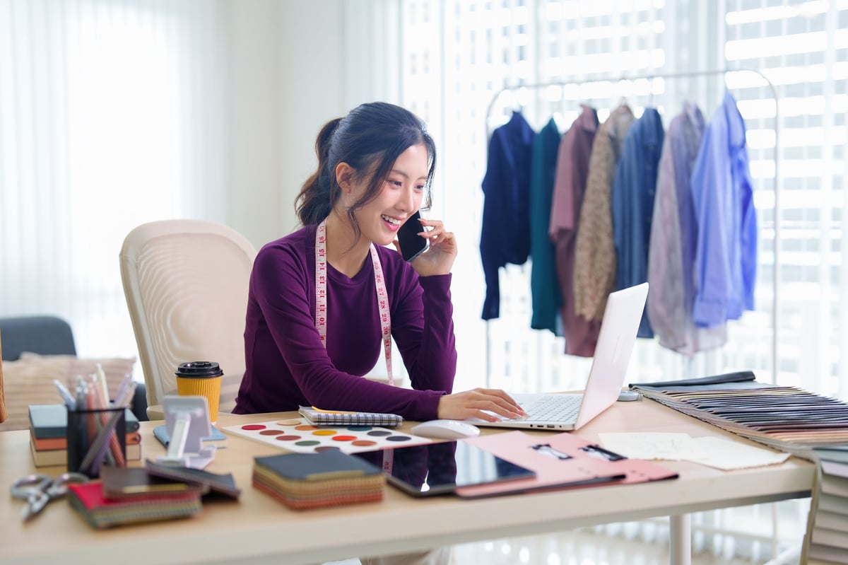 Mujer latina dueña de una pequeña boutique sentada detrás del mostrador, con libretas abiertas y hojas sueltas a la izquierda representando el caos, y una computadora portátil con información organizada a la derecha representando la tranquilidad de tener el control